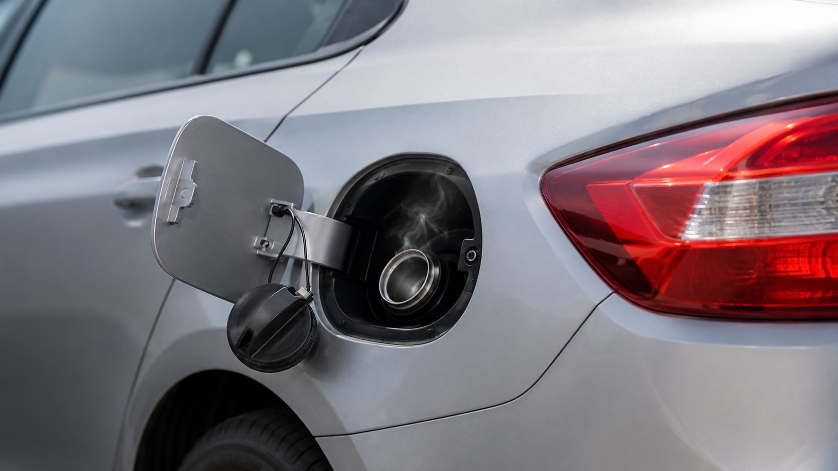 A silver car with an open fuel tank door showing steam rising from the fuel filler neck.